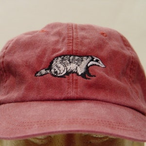 May include: A red baseball cap with an embroidered badger design.
