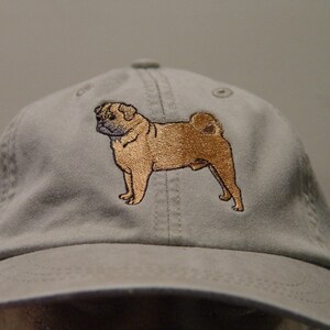 Puede incluir: Una gorra de b&eacute;isbol gris con una imagen bordada de un perro pug marr&oacute;n.