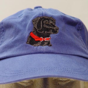 Pu&ograve; includere: Un berretto da baseball blu con un cane ricamato nero che indossa un collare rosso.