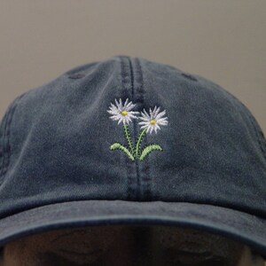 May include: A dark blue baseball cap with a white daisy embroidered on the front.