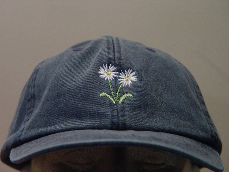May include: A dark blue baseball cap with a white daisy embroidered on the front.