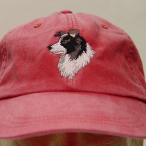 Puede incluir: Una gorra de béisbol roja con un perro border collie negro y blanco bordado en la parte delantera.