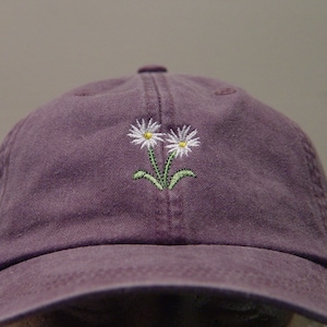 May include: A purple baseball cap with a white daisy embroidered on the front.