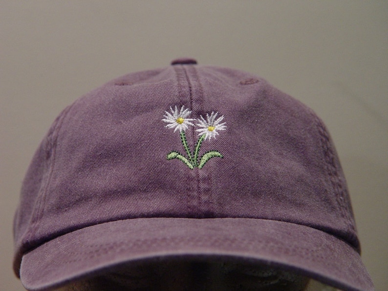 May include: A purple baseball cap with a white daisy embroidered on the front.
