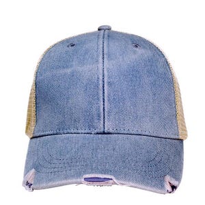 May include: A blue denim baseball cap with a distressed, worn look. The cap features a mesh back in a tan color and a curved brim. The front of the cap has a slightly faded appearance with distressed details near the brim.