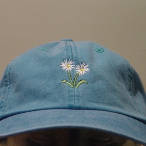 May include: A blue denim baseball cap with two white embroidered daisies.