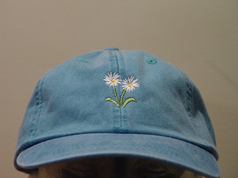 May include: A blue denim baseball cap with two white embroidered daisies.