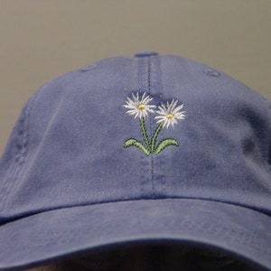 May include: A blue baseball cap with an embroidered design of two white daisies with green stems.