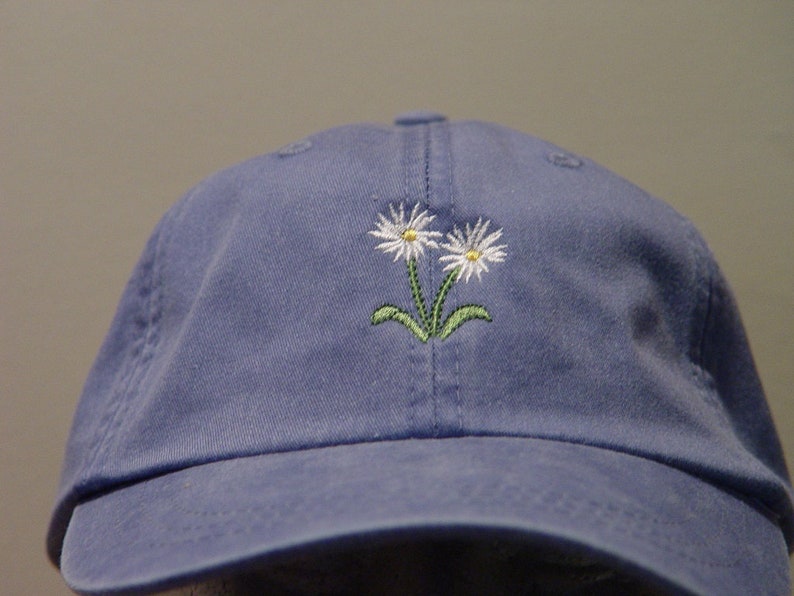 May include: A blue baseball cap with an embroidered design of two white daisies with green stems.