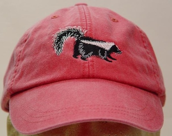 May include: A pink baseball cap with an embroidered black and white skunk on the front.