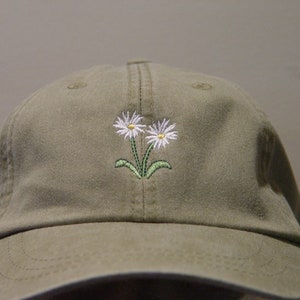 May include: A khaki green baseball cap with two white embroidered daisies with yellow centers and green stems.