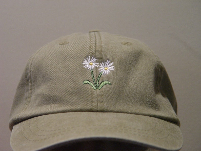 May include: A khaki green baseball cap with two white embroidered daisies with yellow centers and green stems.