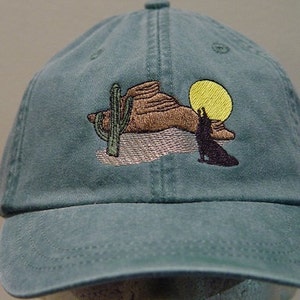 May include: A teal blue baseball cap with an embroidered design of a coyote howling at the moon in a desert landscape with a cactus.