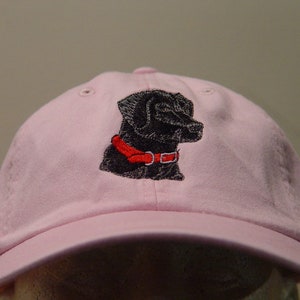 Pu&ograve; includere: Un berretto da baseball rosa con un labrador retriever nero ricamato che indossa un collare rosso.
