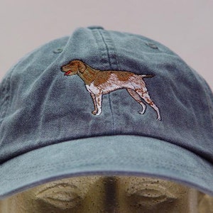 Puede incluir: Una gorra de béisbol de lona azul con un perro marrón y blanco bordado en la parte delantera.