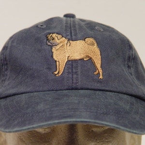 Puede incluir: Una gorra de b&eacute;isbol azul oscuro con una imagen bordada de un pug color canela.