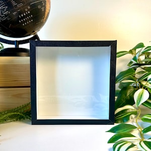 May include: A black picture frame with a white mat and a clear glass front. The frame is sitting on a white surface.