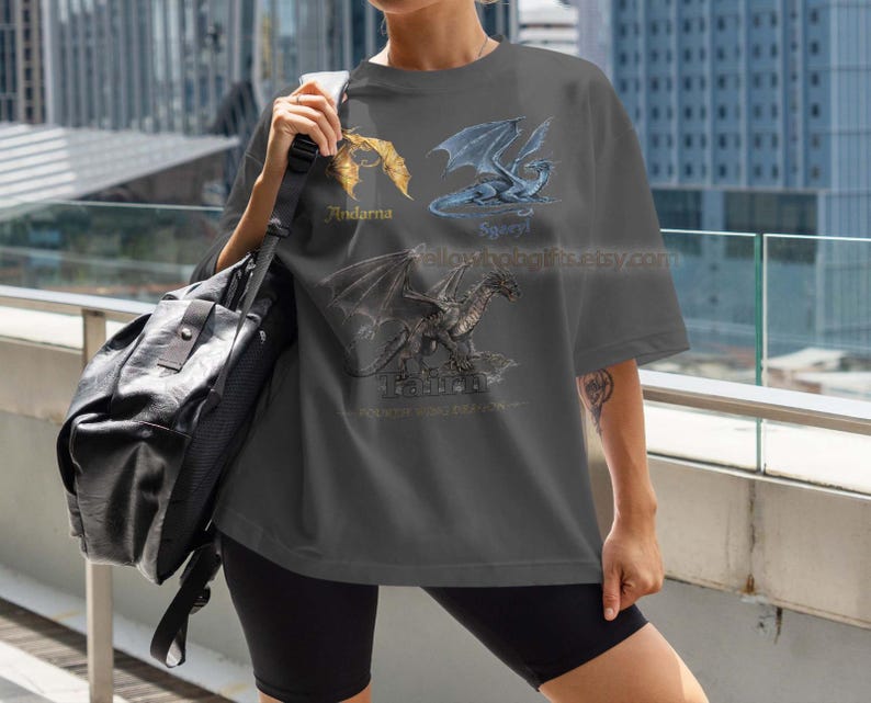 K&ouml;nnte beinhalten: Dunkelgraues T-Shirt mit drei Drachenillustrationen mit den Namen Andarna, Sgaeyl und Tiamat. Das Shirt hat eine lockere Passform und wird mit schwarzen Shorts getragen. Der Etsy-Shop-Name ist auf dem Shirt sichtbar.