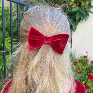 May include: A red velvet bow tied in the hair of a person with long blonde hair.
