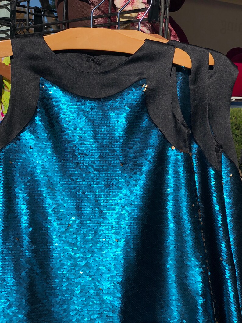May include: A sleeveless sequined dress with a black bodice and a teal blue sequined skirt.