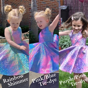 May include: Three girls wearing iridescent tie-dye dresses. The dresses are rainbow shimmer, pink and blue tie-dye, and purple and pink tie-dye.