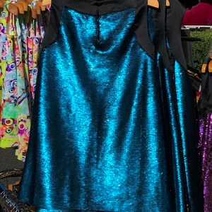 May include: A sleeveless sequined dress with a black neckline and a teal blue color. The dress has a layered skirt.