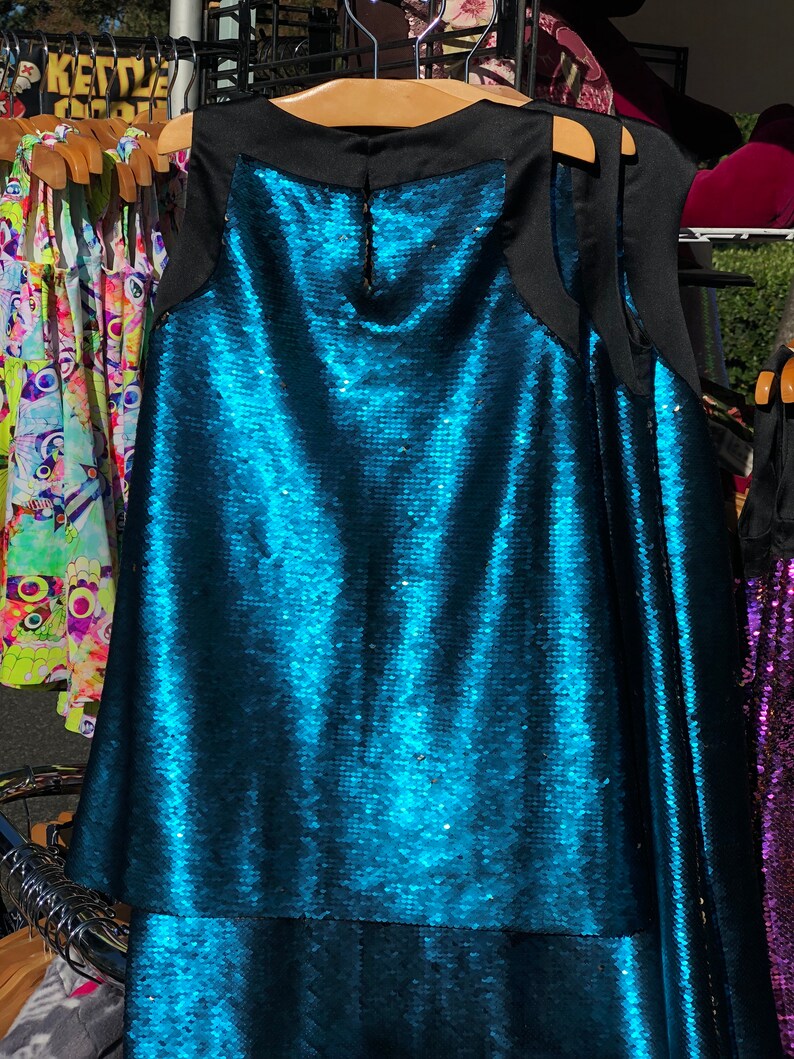 May include: A sleeveless sequined dress with a black neckline and a teal blue color. The dress has a layered skirt.