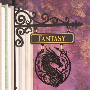 Puede incluir: Letrero de metal negro con la palabra "FANTASY" en letras doradas. Una silueta de dragón aparece debajo. El letrero está colgado frente a una pila de libros. El fondo es de color púrpura y dorado.