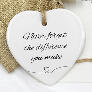 May include: White ceramic heart-shaped ornament with the text "Never forget the difference you make" in black lettering. The ornament is packaged in a small hessian bag.