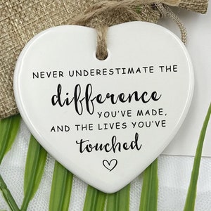 May include: White ceramic heart-shaped ornament with the text "Never underestimate the difference you've made, and the lives you've touched" in black lettering.