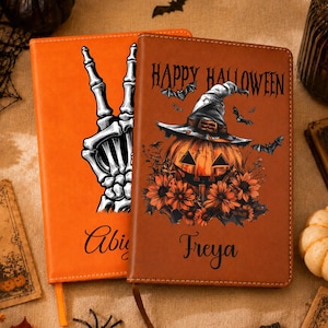May include: Two rectangular journals with leather-like covers. The left journal is bright orange with a black skeleton hand making a peace sign and the name Abigail. The right journal is brown with a jack-o'-lantern wearing a witch hat, sunflowers, bats, the text Happy Halloween, and the name Freya.