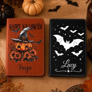 Puede incluir: Dos cuadernos rectangulares con cubiertas de aspecto cuero. La cubierta izquierda es naranja con una calabaza con sombrero de bruja, girasoles, murciélagos y el texto "HAPPY HALLOWEEN" y "Freya". La derecha es negra con murciélagos blancos, estrellas y "Lucy".
