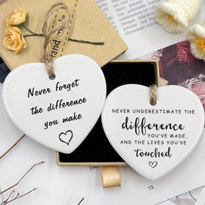 May include: Two white heart-shaped ornaments with black text and a jute string. One says "Never forget the difference you make" and the other "Never underestimate the difference you've made, and the lives you've touched."