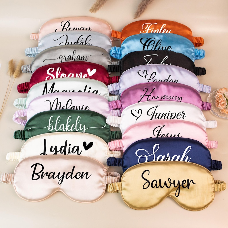 May include: A collection of personalized satin sleep masks in various colors, including pink, blue, and green. Each mask features a name in elegant script. The masks have elastic bands for a comfortable fit and are designed for eye coverage.