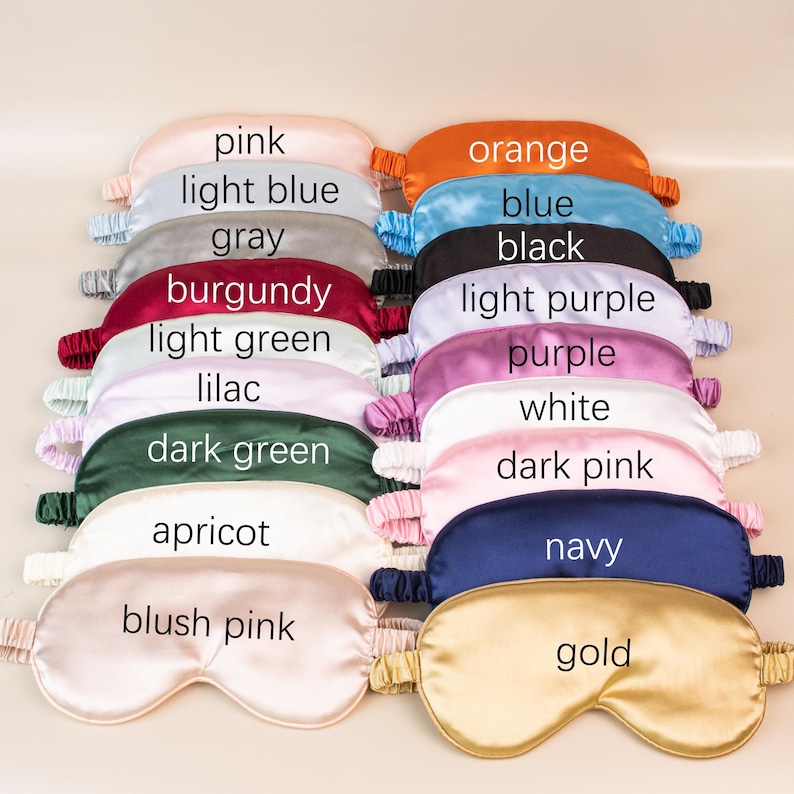 May include: A collection of silk sleep masks in various colors, including pink, light blue, gray, orange, blue, black, light purple, burgundy, light green, lilac, purple, white, dark green, dark pink, apricot, navy, blush pink, and gold. Each mask has an elastic strap.
