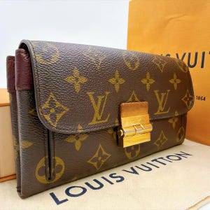 Pode incluir: Uma carteira Louis Vuitton castanha com o icónico padrão de monograma em dourado. A carteira tem uma forma retangular com uma aba dobrável fixada por um fecho de metal polido em tom dourado. Os painéis laterais são de cor bordô texturizada.