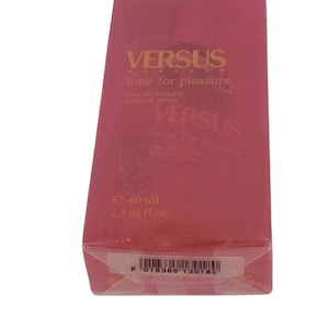 May include: A pink box with a gold label that reads "VERSUS time for pleasure eau de toilette natural spray". The box also has a barcode and the text "e 40 ml 1.3 us fl.oz."