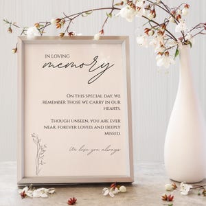 May include: A framed sign with the words "In Loving Memory" in elegant script. The sign includes a heartfelt message about remembrance and love. A white vase with floral arrangements is to the right of the sign.