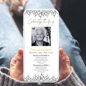 May include: A smartphone displaying a memorial announcement. The design features a black and white photo of a woman, with text that reads "Celebrating the life of Amanda Rogers." Floral accents frame the top and bottom.