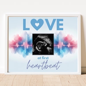 May include: Framed print featuring the word "LOVE" in blue, a heart symbol, and an ultrasound image. The text "at first heartbeat" is written in a cursive font. The background has watercolour-style pink and blue accents.