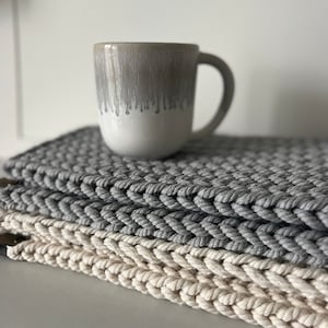 May include: A white ceramic mug with a gray glaze and a drip effect sits on top of two gray and white crocheted coasters.