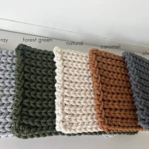 May include: Five knitted squares in different colors: light gray, forest green, natural, caramel, and charcoal. The squares are arranged horizontally, with the light gray square on the left and the charcoal square on the right.
