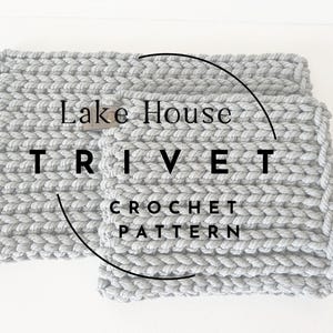 May include: Two grey crochet trivets, one rectangular and one square, are shown on a white surface. The text "Lake House TRIVET CROCHET PATTERN" is overlaid. The trivets are made of thick, textured yarn, suitable for kitchen use.