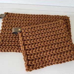 May include: Two brown knitted pot holders with leather loops. The pot holders are made of thick, chunky yarn and have a textured surface.