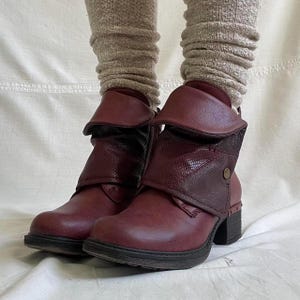 Peut inclure: Bottes de cheville bordeaux avec un revers. Les bottes ont un empiècement texturé et un petit talon. Les bottes sont portées avec des chaussettes beige côtelées.
