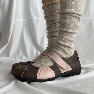 Könnte beinhalten: Braune und rosa Mary Jane-Schuhe mit Riemenverschluss. Die Schuhe haben eine dunkelbraune Sohle und eine hellbraune Spitze. Die Schuhe werden mit beigefarbenen Beinwärmern getragen.