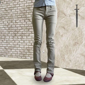 May include: Pale grey denim jeans with a classic five-pocket design. The jeans are worn with burgundy Mary Jane shoes. The person is wearing a light blue button-down shirt. The background features a brick wall and a textured wall.