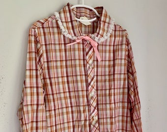 May include: A long-sleeved, plaid button-up shirt with a pink bow and white lace trim on the collar and cuffs.