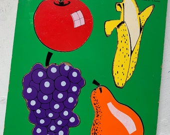 May include: A wooden puzzle with the text "fruits I like" and four pieces: a red apple, a yellow banana, a purple bunch of grapes, and an orange pear. The puzzle is made by Playskool and has 4 pieces.