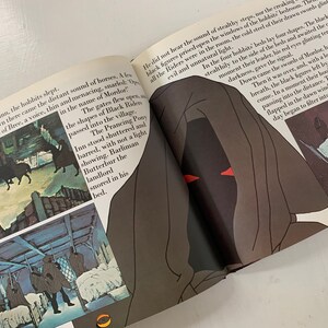 May include: A book open to a page with an illustration of a hooded figure with red eyes. The text on the page reads "The gates flew open in the name of Mordor." The illustration is in a dark, shadowy style.